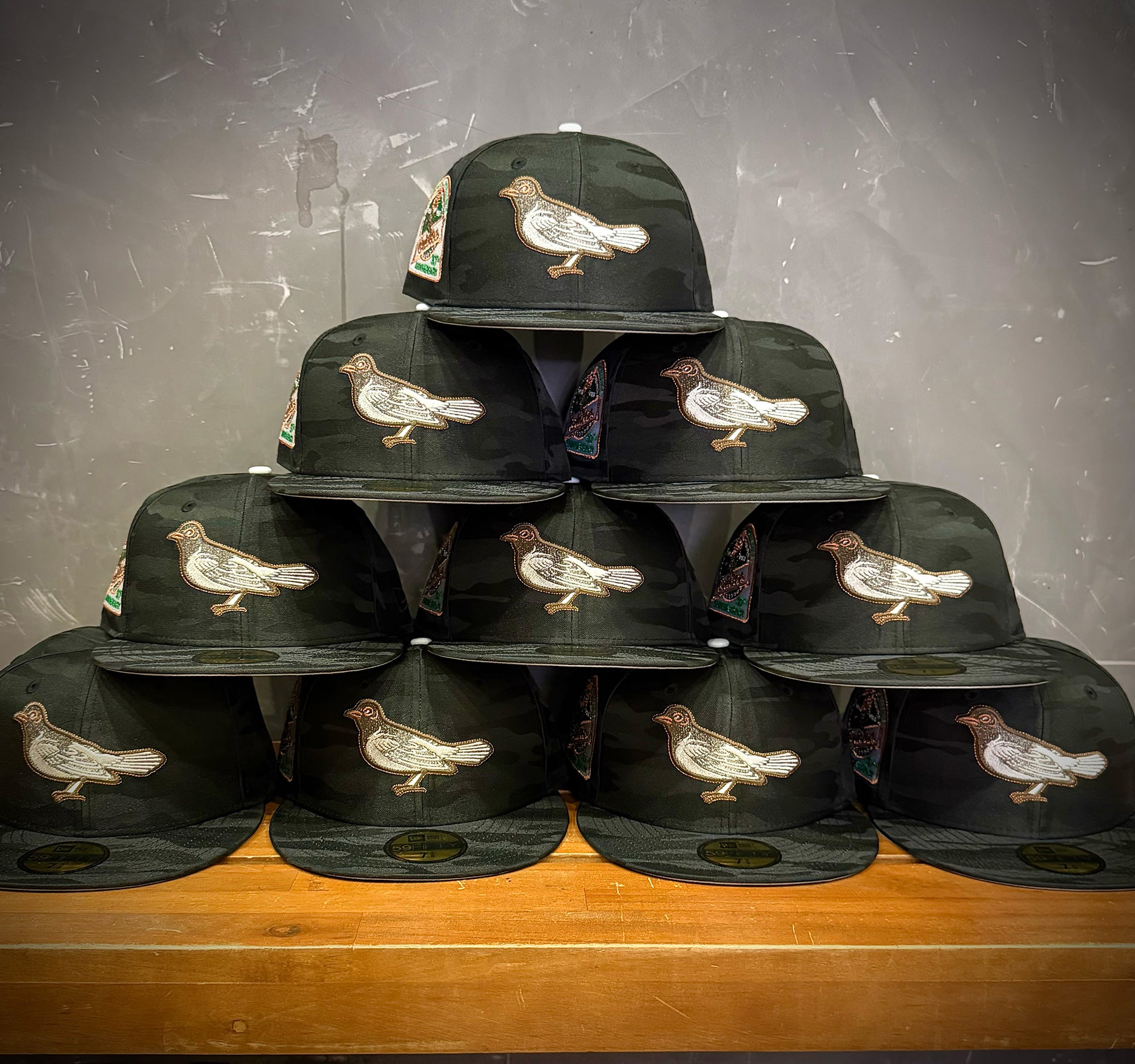 Highlark Baltimore Orioles 3.0 pyramid stack front view, multiple hats showing front bird logo on tonal black camo crowns