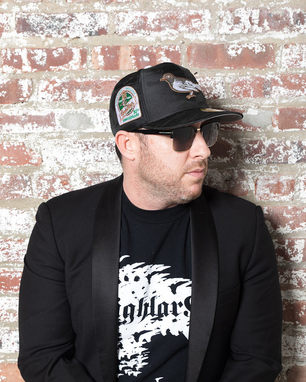 Highlark Baltimore Orioles 3.0 fitted cap on model against brick wall, 30th Anniversary sidepatch visible with Highlark Collective tee and uxedo blazer styling